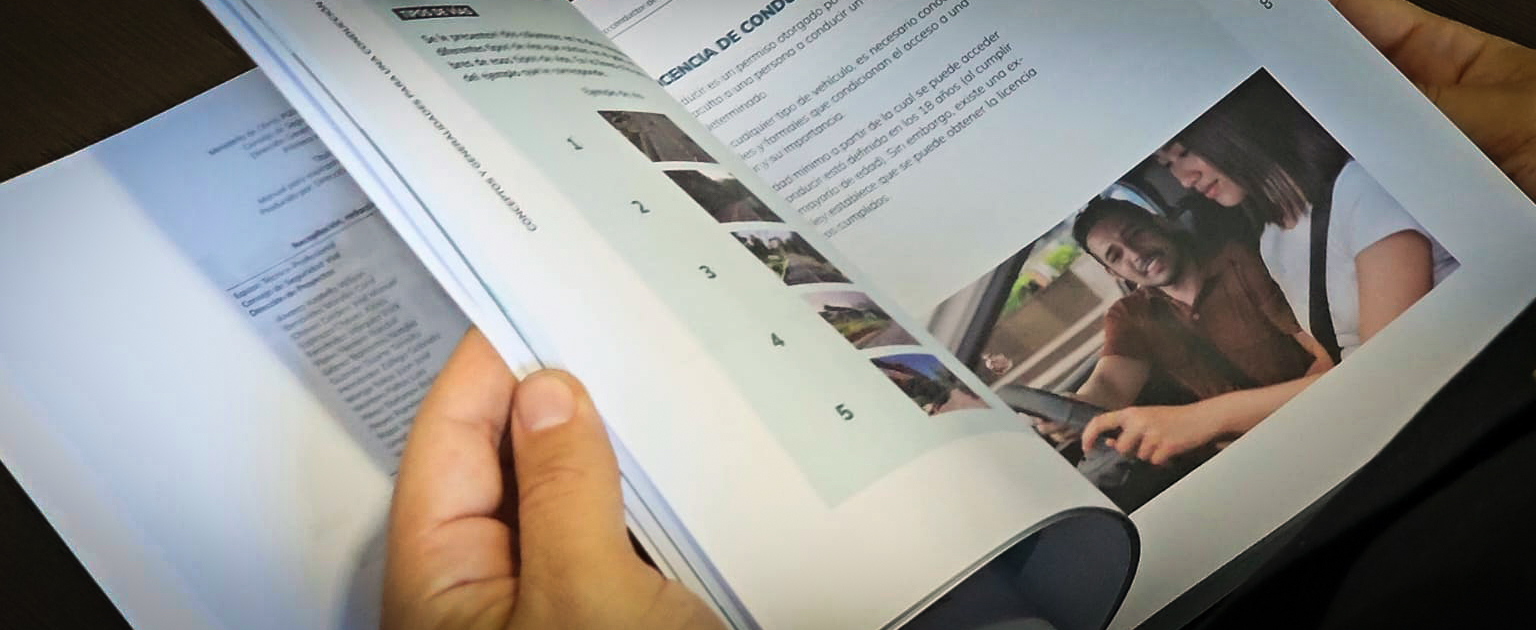Persona pasa páginas del nuevo manual del conductor, donde se observan textos, imágenes ilustrativas y una sección sobre licencias de conducir con fotografías y pasos enumerados.