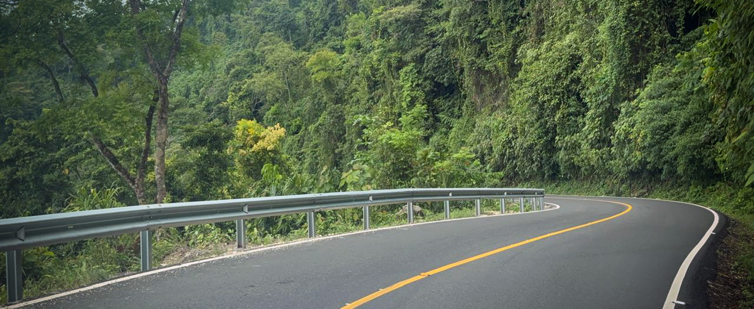 Tramo mejorado del proyecto Fila de Cal, con carretera asfaltada, demarcación horizontal y barreras de seguridad metálicas. La vía atraviesa una zona montañosa rodeada de abundante vegetación.