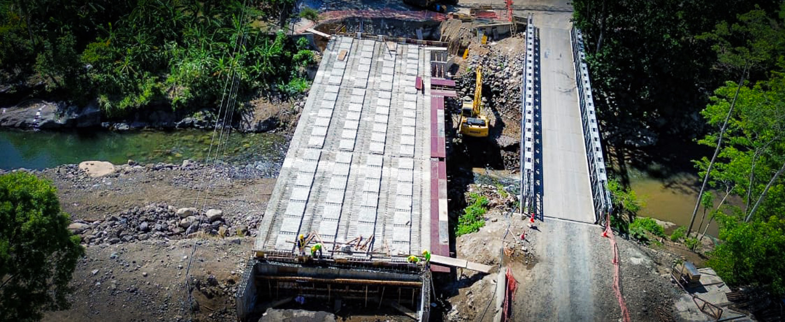 Vista aérea de la construcción del nuevo puente sobre el río Guacimal, con prelosas, maquinaria pesada y un puente provisional en uso