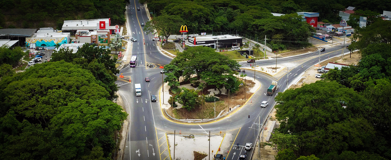 Vista aérea de la intersección de Nicoya, donde convergen varias vías de circulación vehicular. La imagen muestra carriles recientemente construidos o rehabilitados, áreas de giro canalizadas, demarcación horizontal y una isla central con abundante vegetación. Alrededor de la intersección se observan establecimientos comerciales, zonas boscosas y vehículos transitando por la red vial mejorada.