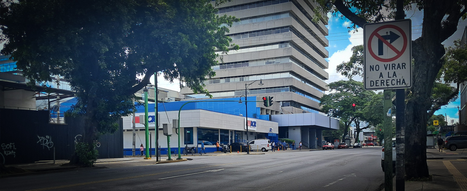 Vista del Paseo Colón en San José, con una intersección urbana, edificios comerciales y una señal de tránsito que prohíbe girar a la derecha