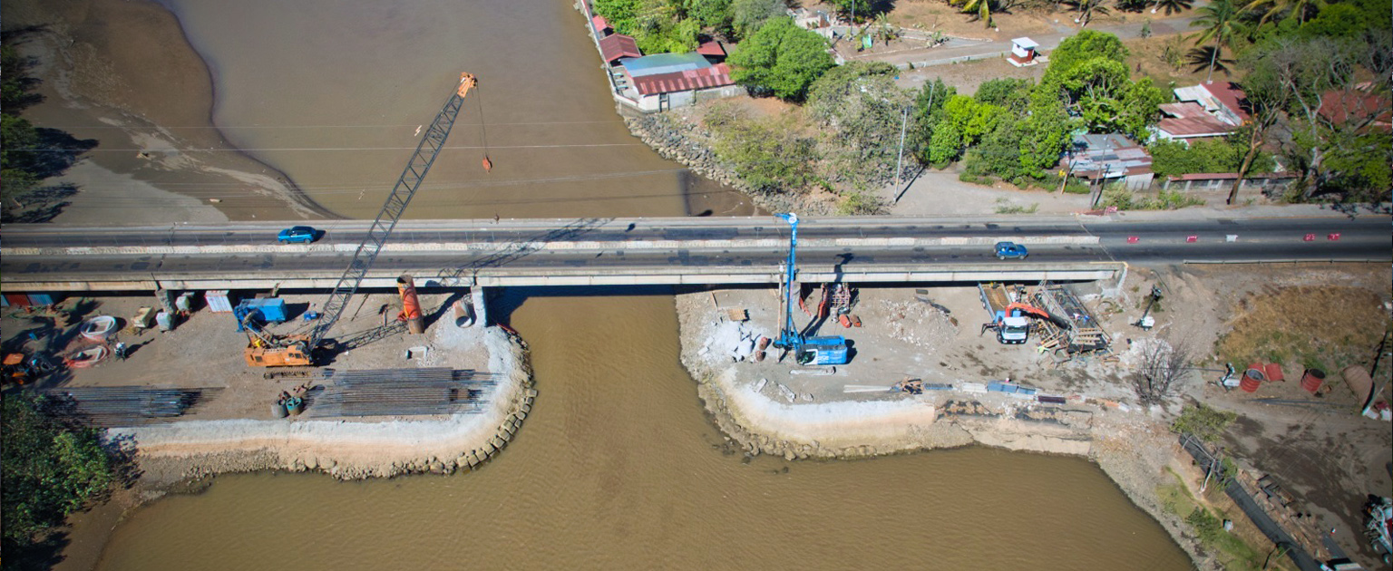 Foto aérea del puente sobre Río Barranca. Se observa ambos lados del río y maquinaria trabajando.
