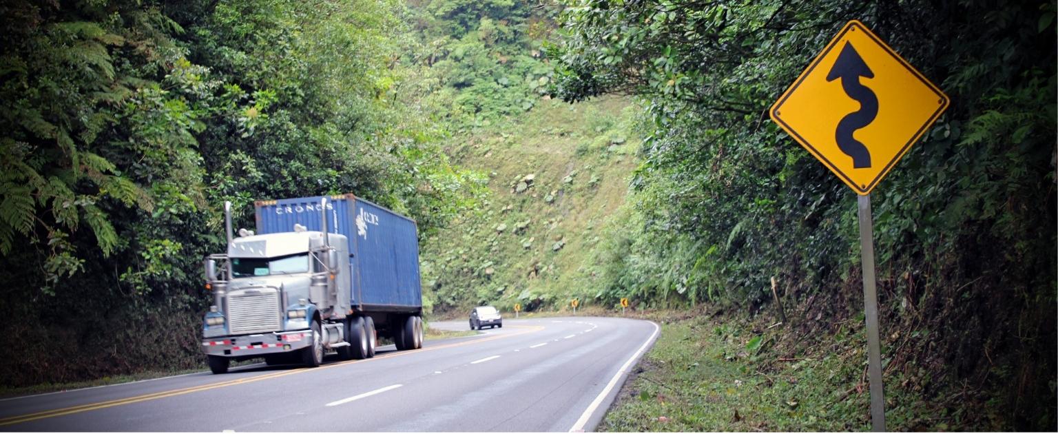 Ruta 32, hay una señal vertical y amarilla que indica curvas en la carretera. Además de un camión y vehículo.emás 