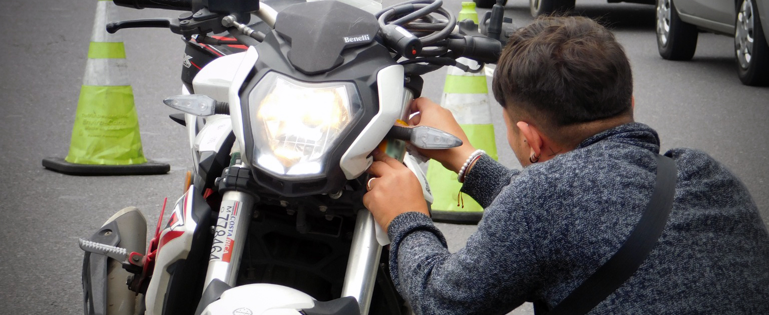 Hombre de espalda, agachado, colocando adhesivo de marchamo en la parte frontal de la motocicleta