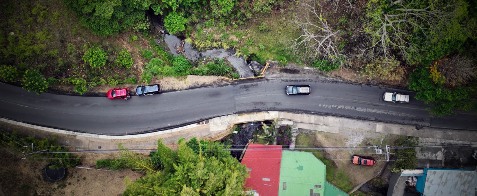 Foto aérea se visualiza la carretera entre montañas, con dos vehículos en ellos.