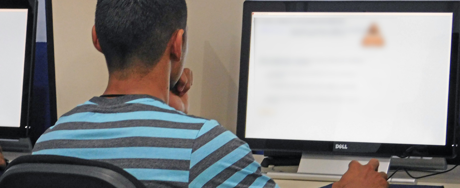 Hombre con camisa de rayas, sentado frente a computadora, realizando prueba.