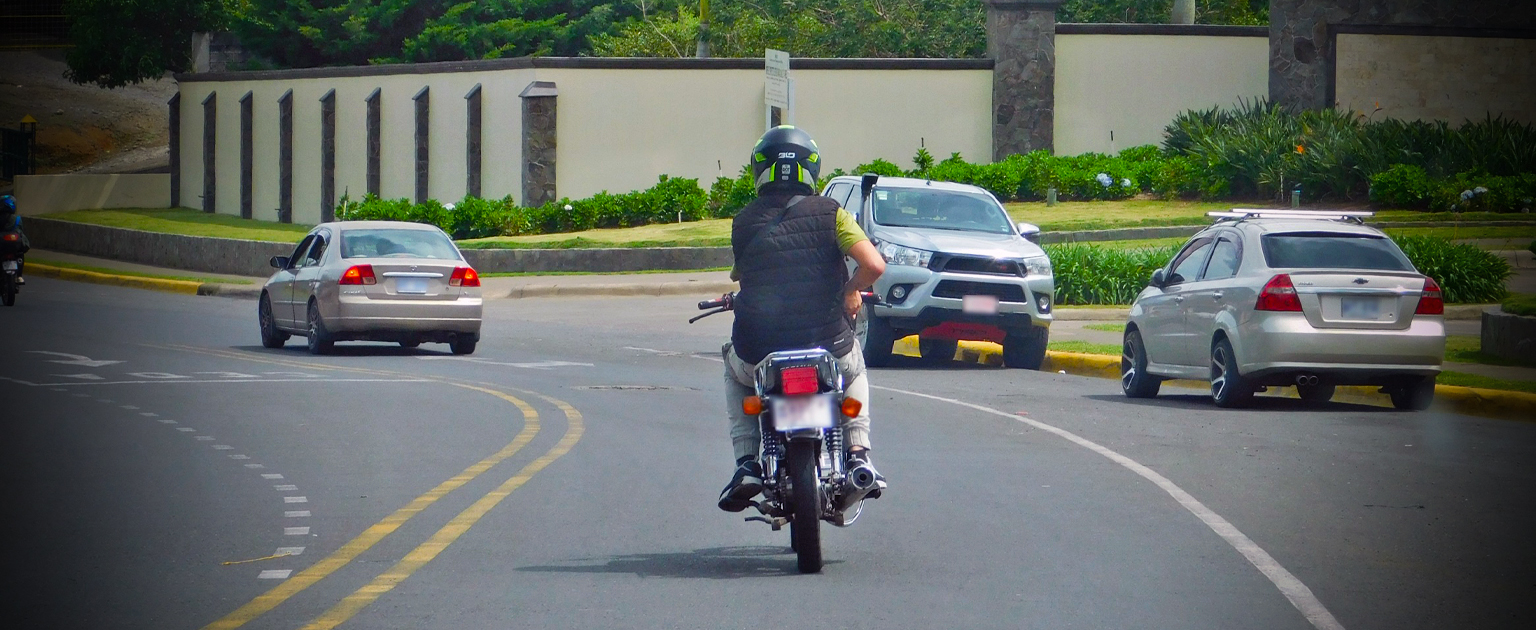 Fotografía que muestra una persona de espaldas circulando en motocicleta junto con otros vehículos