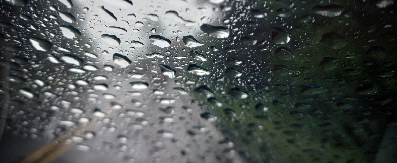 Fotografía que muestra el parabrisas delantero de un auto llego de gotas de agua de lluvia. La foto está tomada desde el interior del vehículo.