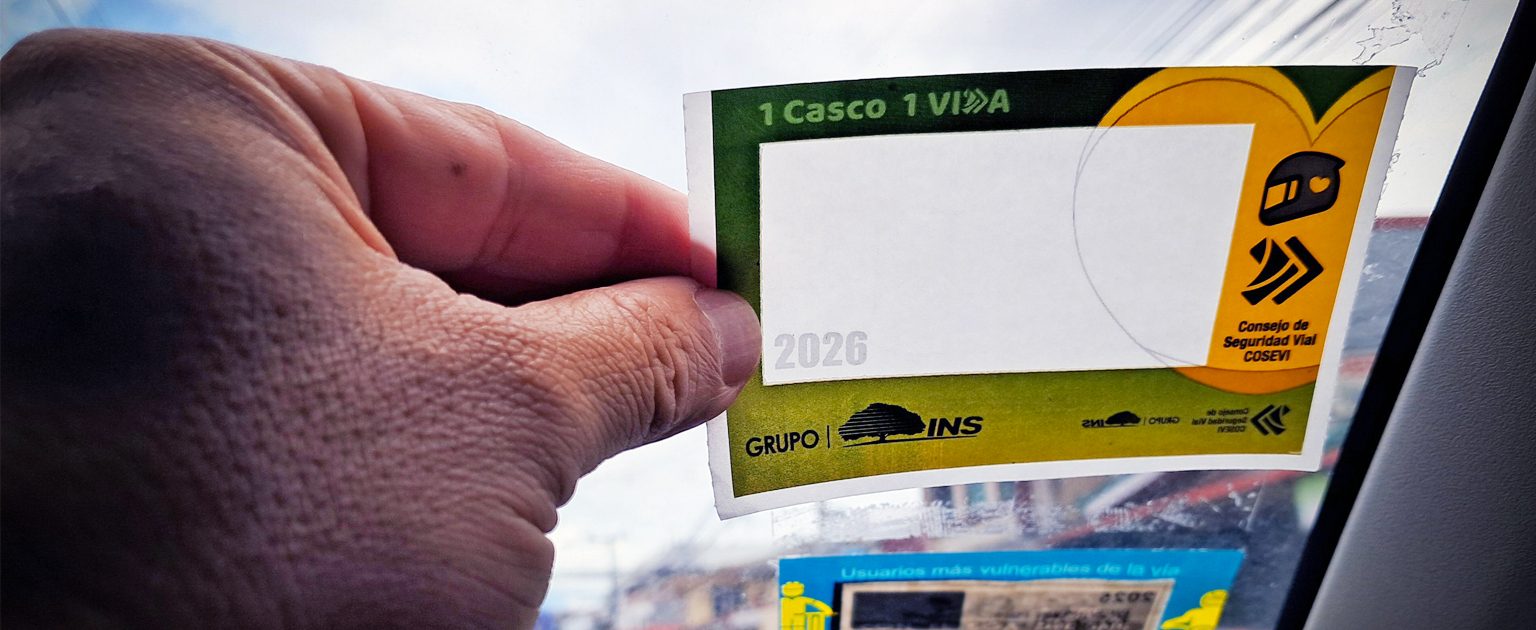 Fotografía que muestra la mano de una persona colocando el marchamo del parabrisas de carro