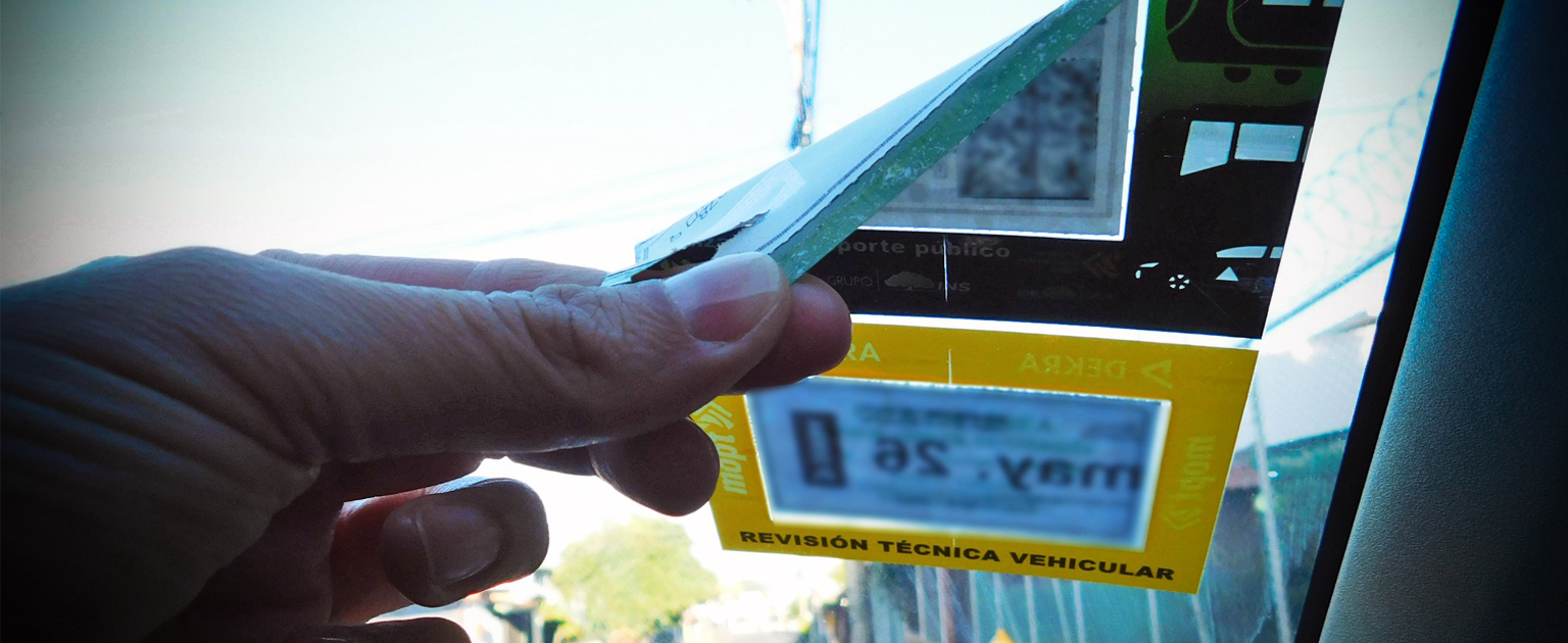 Fotografía que muestra la mano de una persona retirando el marchamo del parabrisas de carro