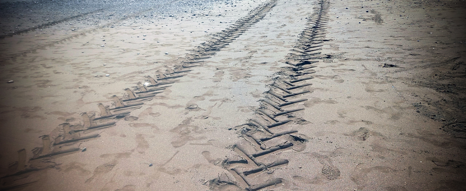 Fotografía que muestra las huellas de un vehículo sobre la arena de una playa