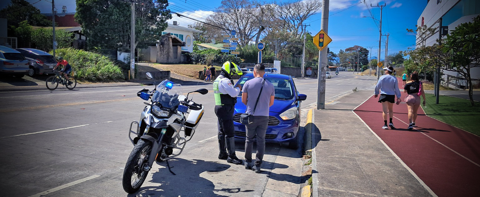 Fotografía que muestra a un oficial de tránsito confeccionando una boleta a un chofer que tiene su carro mal estacionado