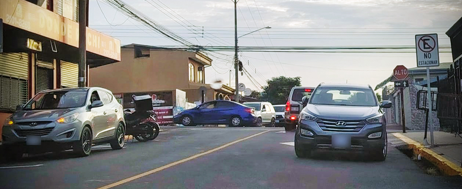 Vehículos estacionados en una calle urbana junto a una señal de prohibición de estacionamiento.