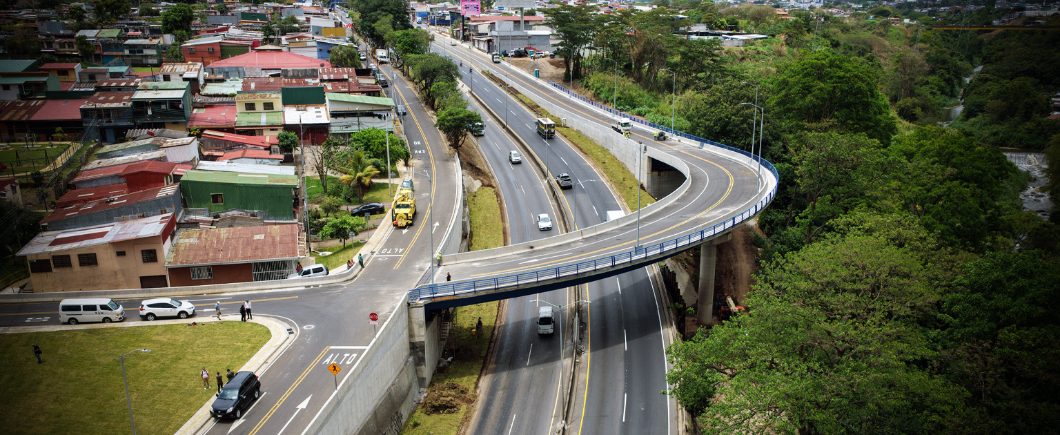 Paso elevado en Hatillos con rampa curva elevada que conecta vías principales sobre la carretera Circunvalación, rodeado de viviendas y vegetación, con tránsito vehicular activo