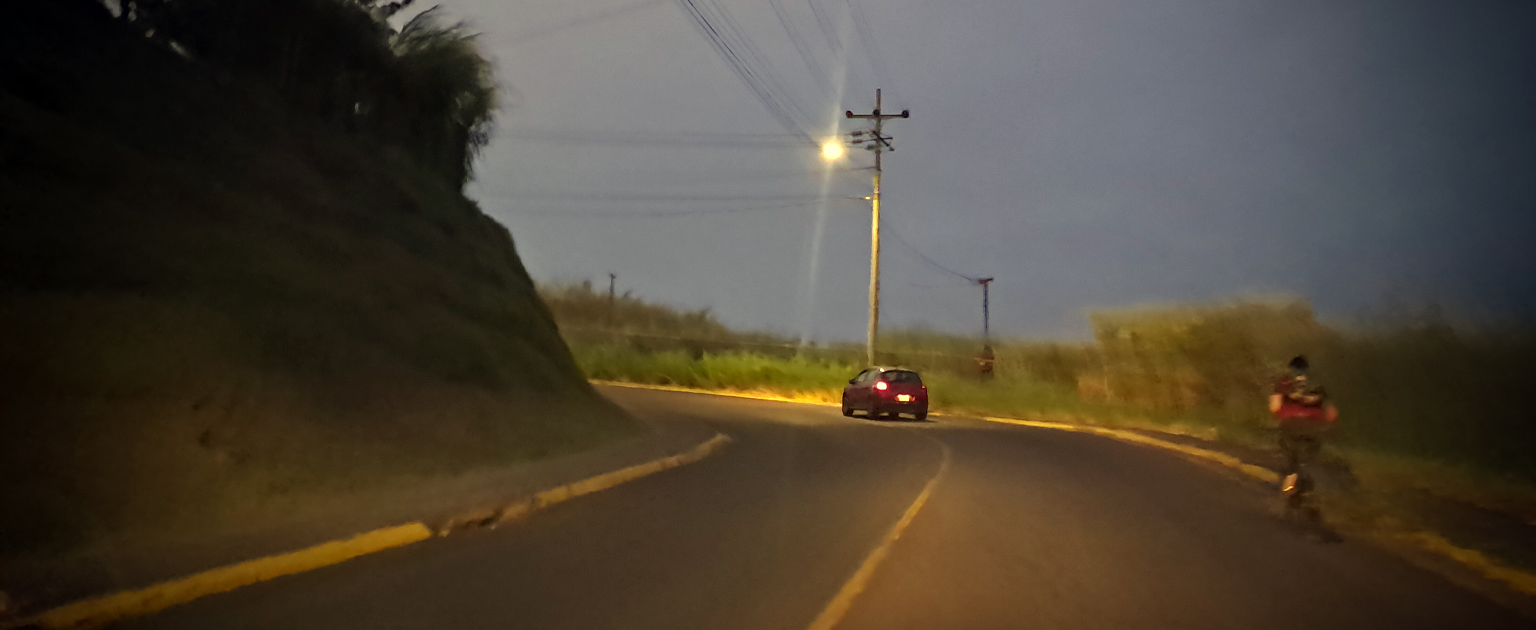 Fotografía que muestra un vehículo y una persona caminando a la derecha de la vía, es de noche