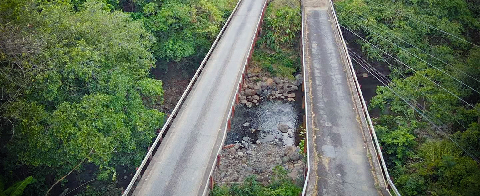 Vista aérea del puente sobre el río Machuca, compuesto por dos estructuras paralelas que permiten el paso vehicular sobre el cauce.