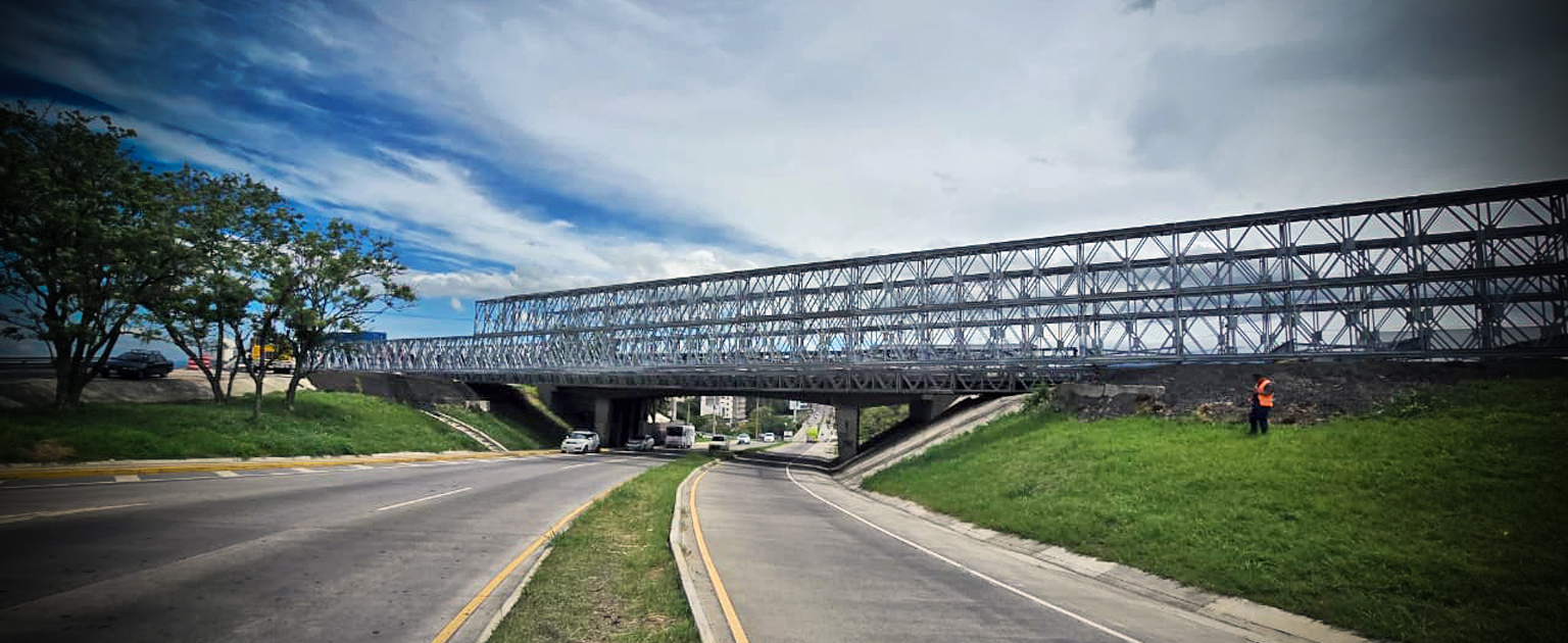 Puente modular en las inmediaciones del Aeropuerto Juan Santamaría, que cruza sobre la Radial Alajuela; se observa la estructura del puente, áreas verdes a los lados y tránsito de vehículos bajo el puente