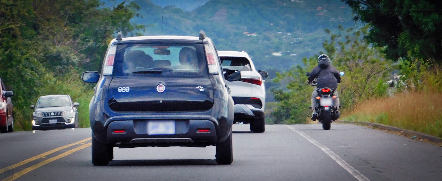 Fotografía que muestra varios vehículos y una moto circulando en una acera