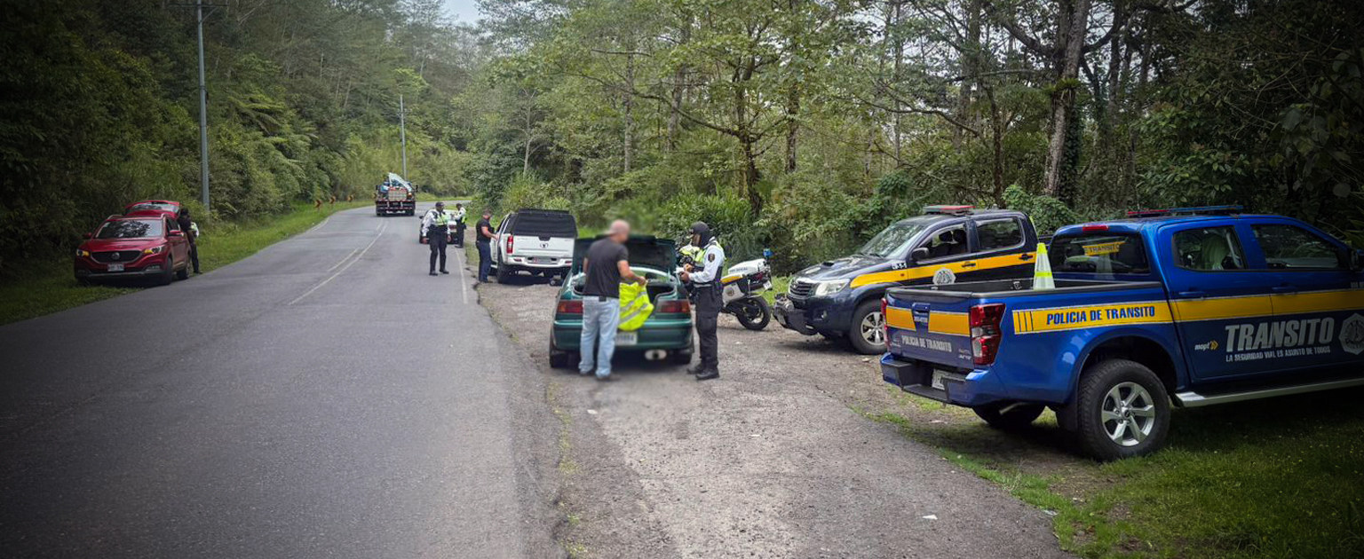 Operativo de control vial en una carretera rodeada de vegetación. Varias unidades de la Policía de Tránsito y motocicletas se encuentran estacionadas en el borde de la vía mientras oficiales realizan inspecciones a vehículos