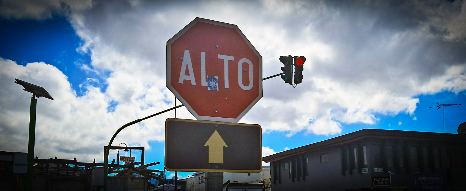 Fotografía que muestra en primer plano una señal de Alto y de fondo un semáforo