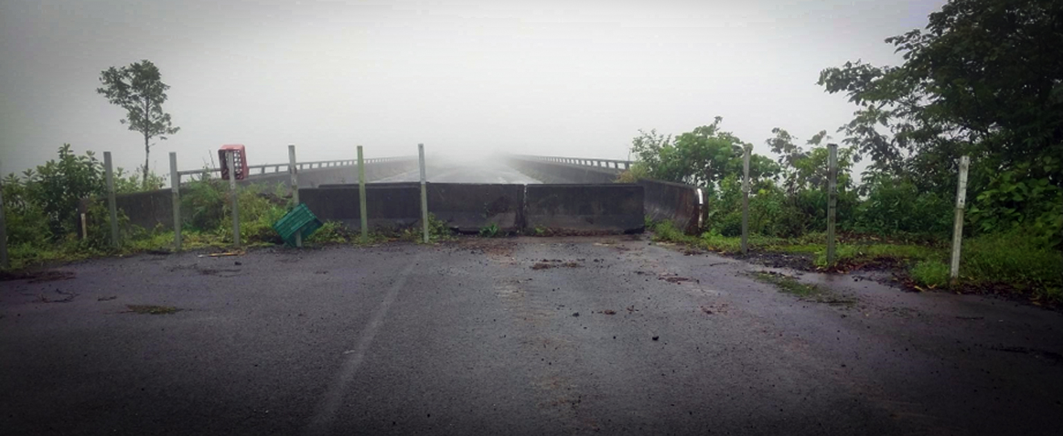 Puente vehicular Tapezco cerrado al tránsito mediante barreras de concreto colocadas en uno de sus accesos. La escena muestra la carretera húmeda rodeada de vegetación, con densa neblina que reduce significativamente la visibilidad sobre la estructura. 