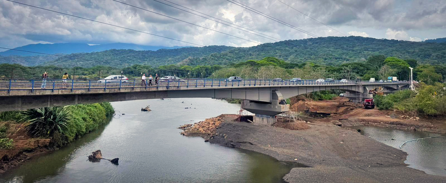 Puente vehicular sobre el río Tárcoles, con personas y tráfico, rodeado de zona boscosa y montañas