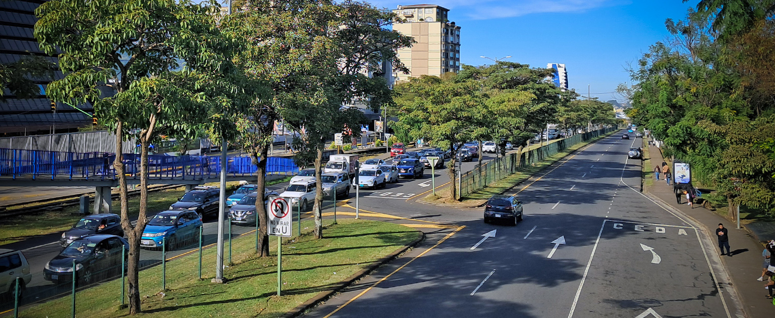 Vista de la Ruta Nacional 27 en las inmediaciones de la Contraloría General de la República, se muestran varios carriles, tránsito vehicular, árboles a ambos lados y peatones en la acera